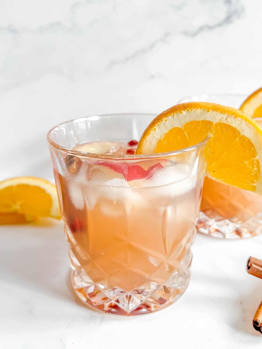 Apple Cider Cocktail in two cups with orange slices on the cups.