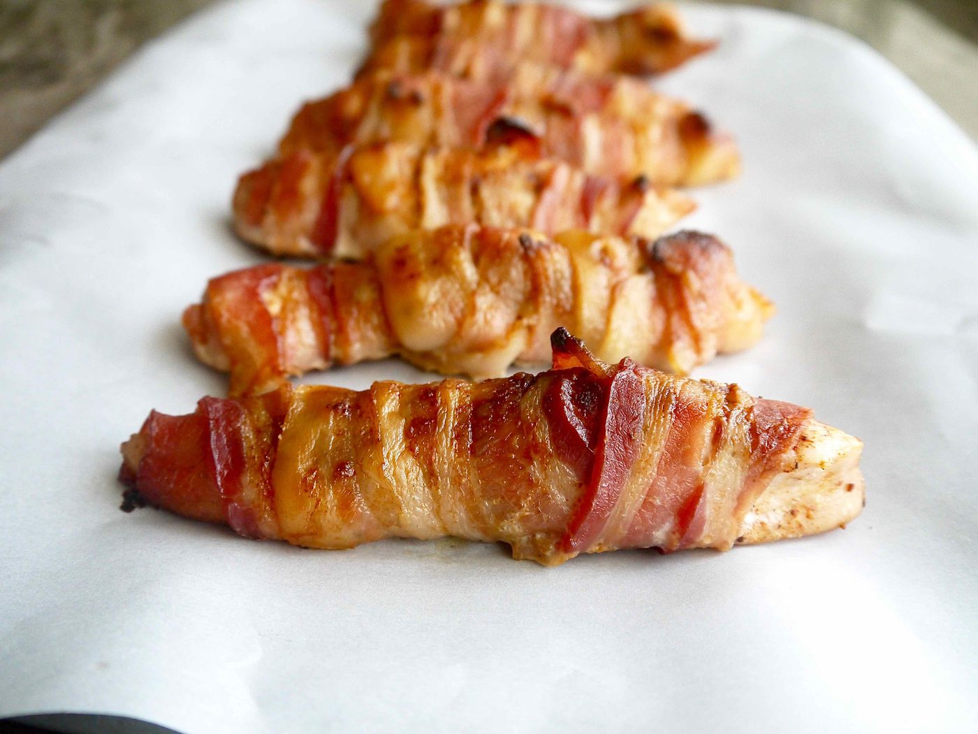 Chicken tenders wrapped in bacon on a pan.
