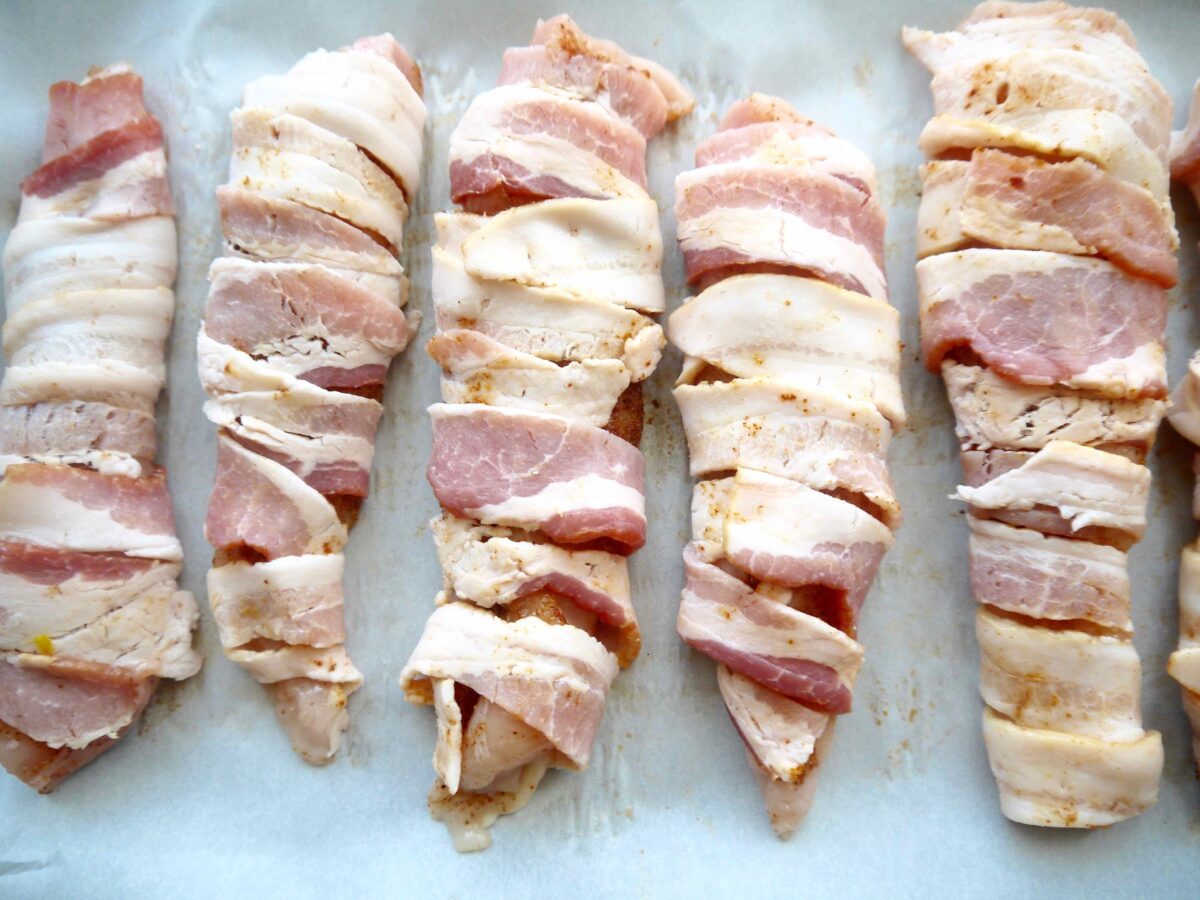 Raw chicken wrapped in bacon before baking.