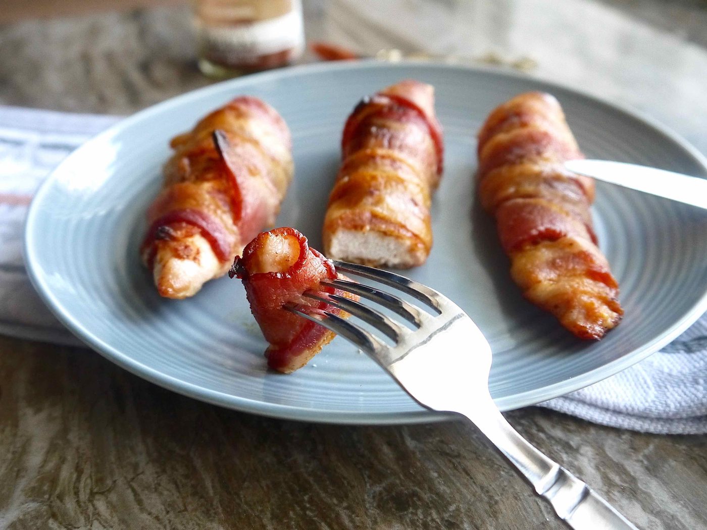 Keto bacon wrapped chicken on a plate with a fork and knife.