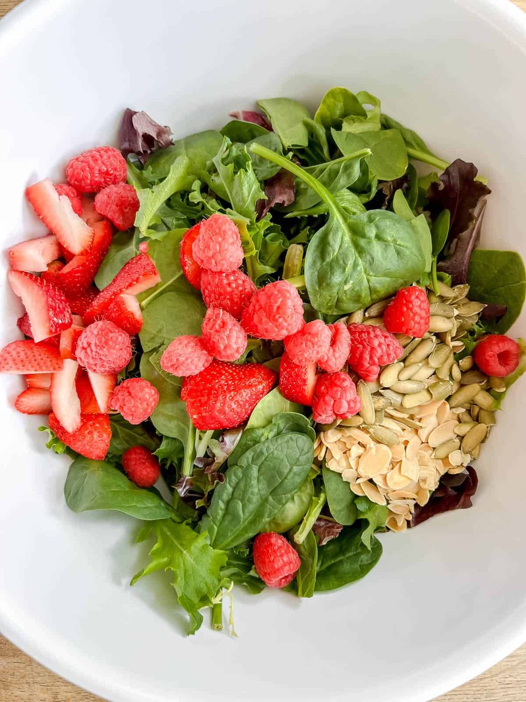 Salad with berries, almonds and pumpkin seeds on top.