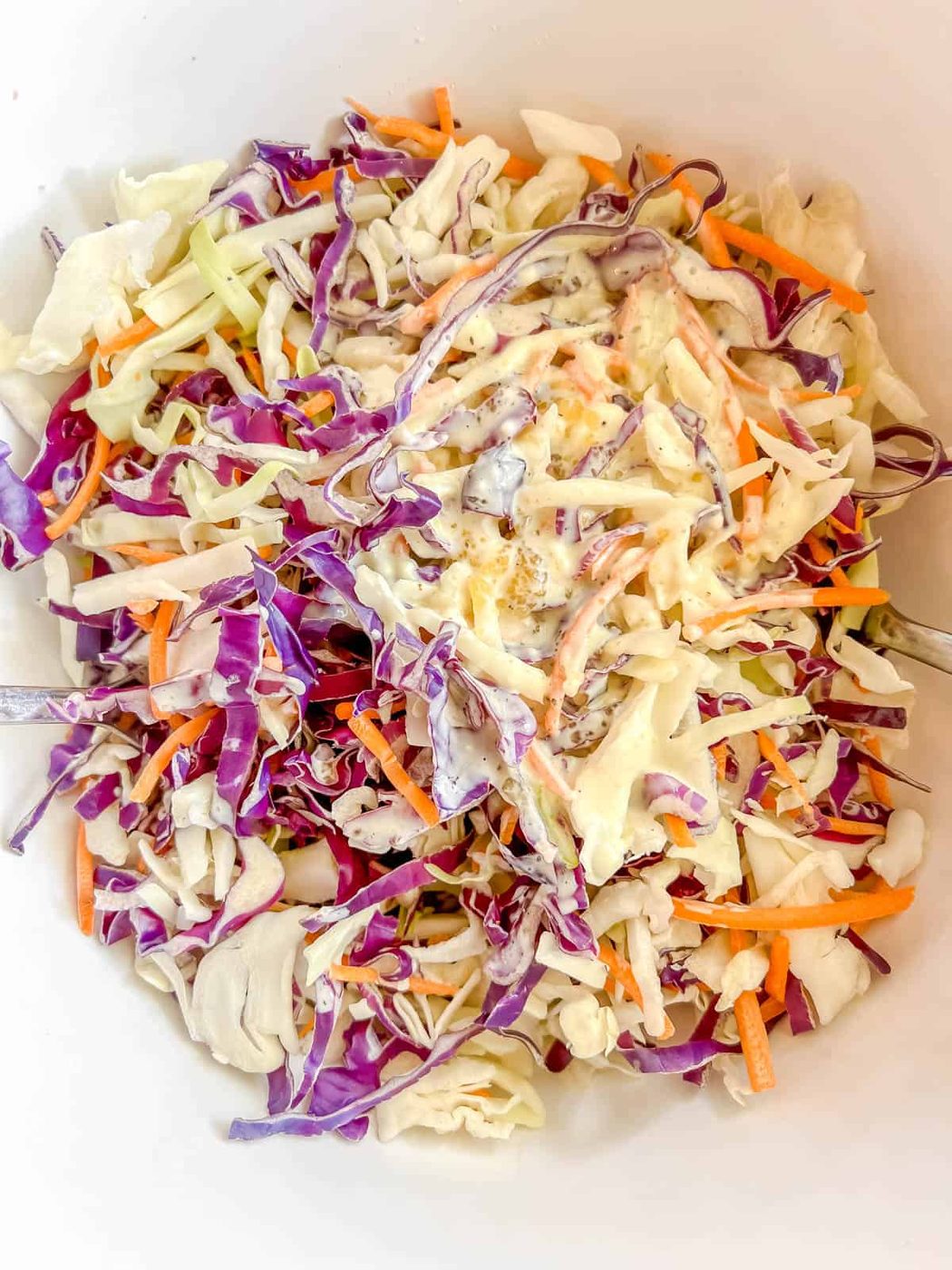 Cabbage, carrots and dressing in a bowl.