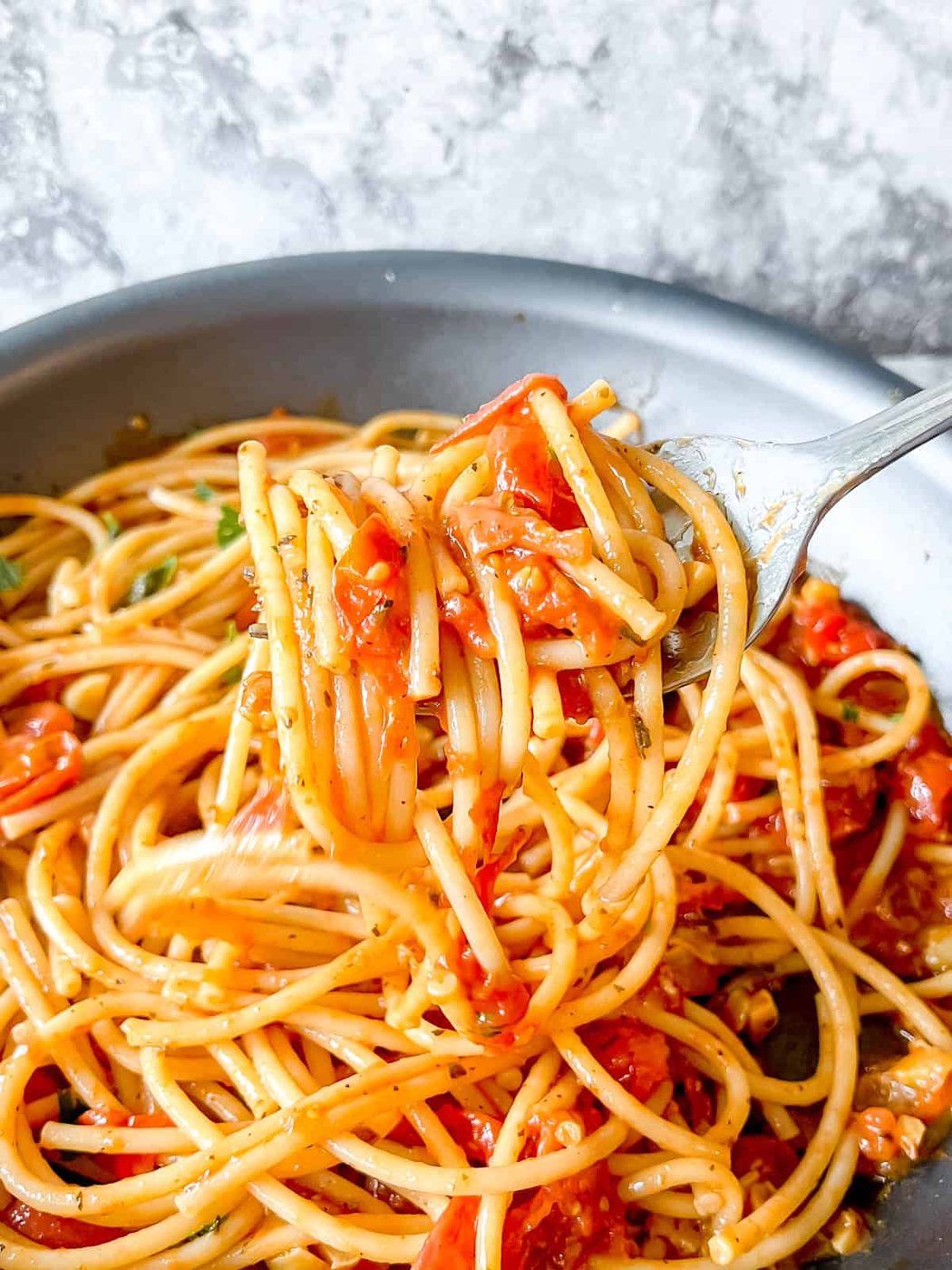 Cherry tomato sauce mixed into pasta in a pan.