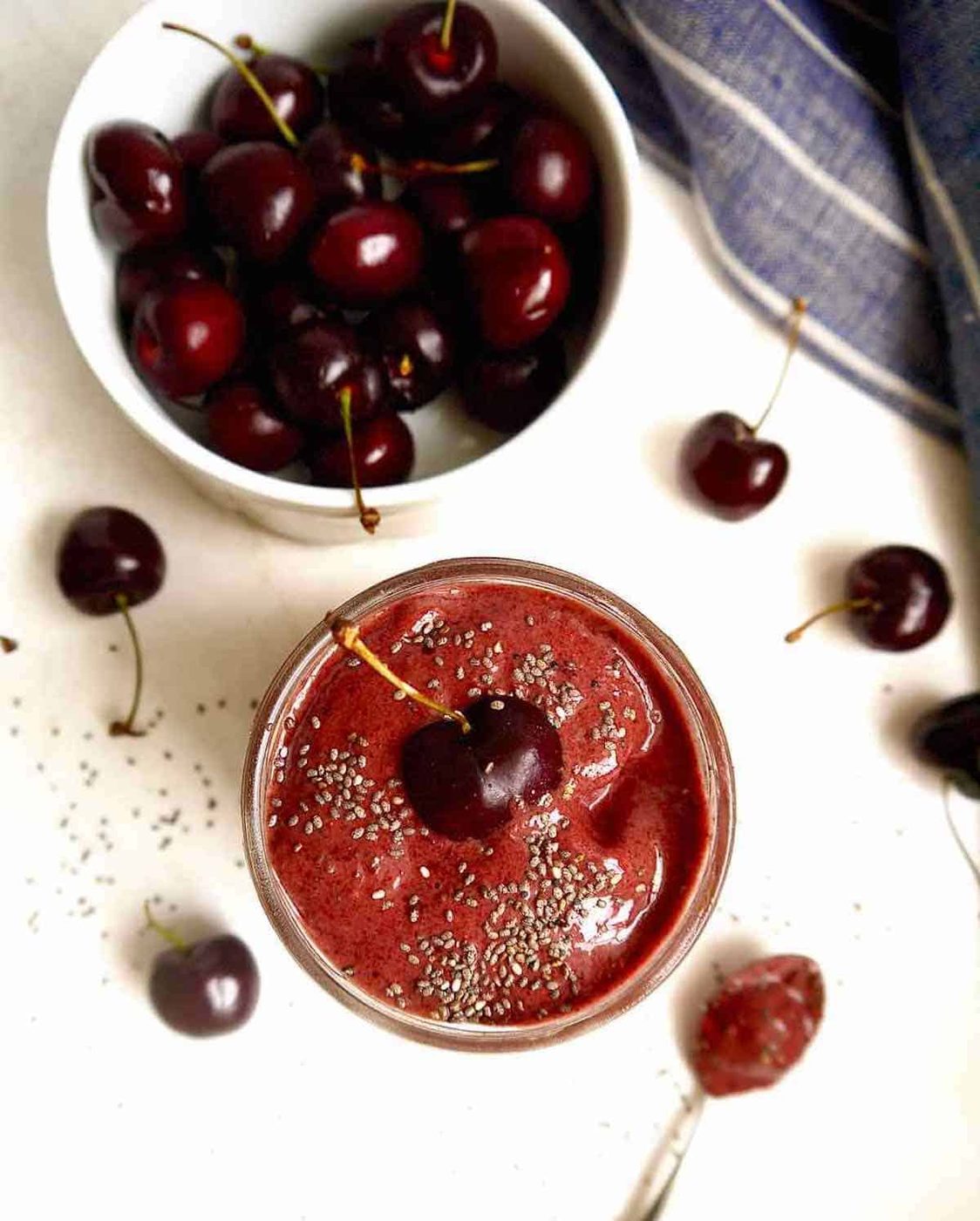 Cherry banana smoothie in a jar with a bowl of cherries next to it.