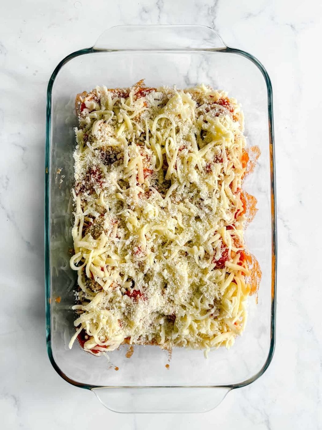 Chicken parm meatballs covered in cheese before baking the cheese.