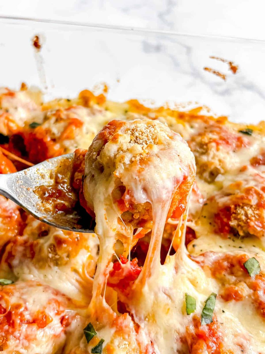 A gooey cheesy chicken parm meatball being lifted out of the dish.