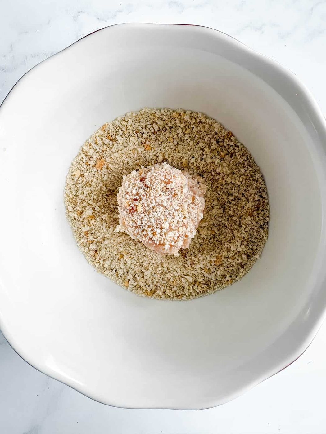 A chicken meatball rolled in a bowl of breadcrumbs.