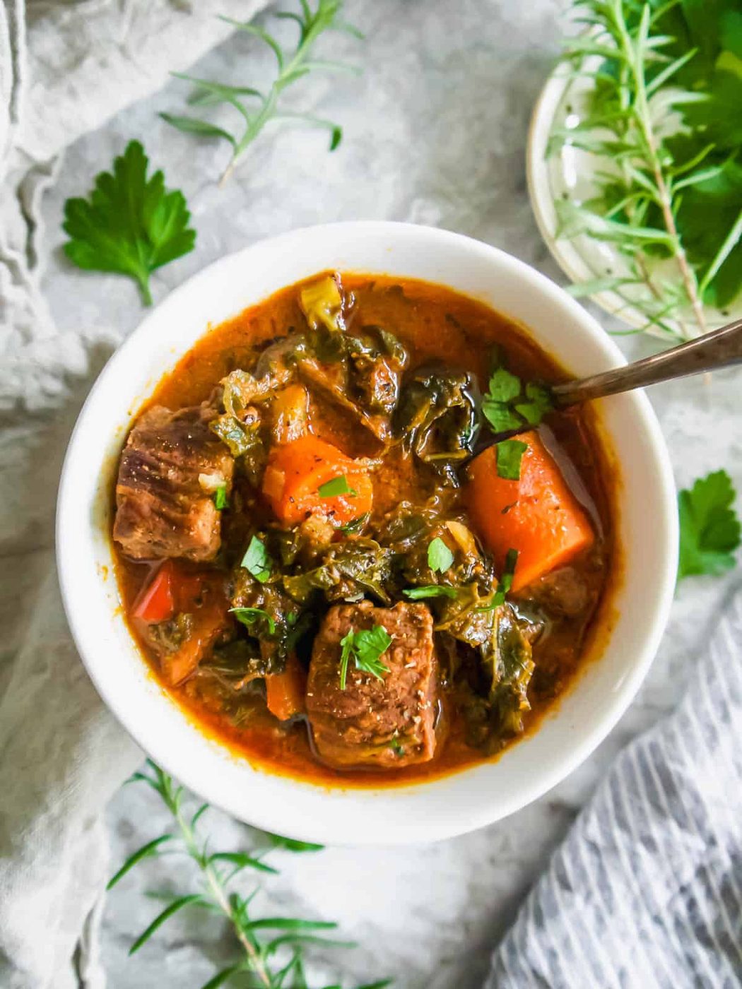 Beef Kale and tomato stew in a large bowl with a spoon in it.