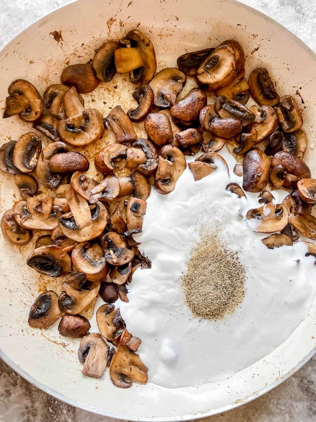 Coconut cream and pepper added to cooked mushrooms in a pan.