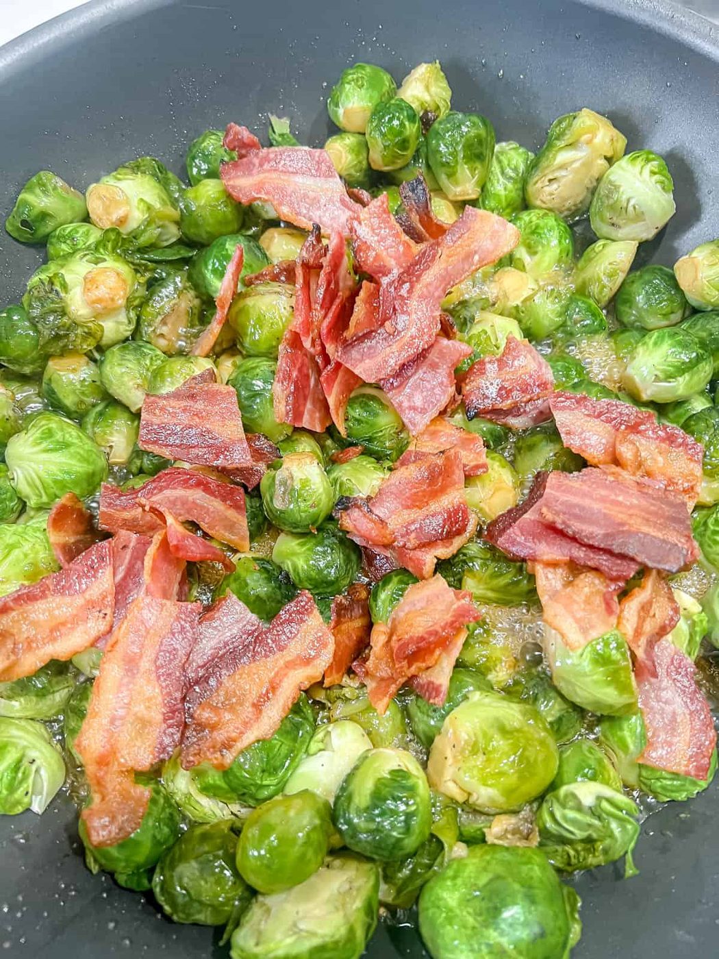 Bacon added to brussels sprouts in frying pan.