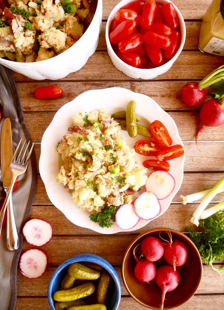 Satisfying french potato salad on a plate with tomatoes, radishes, and cornichons.