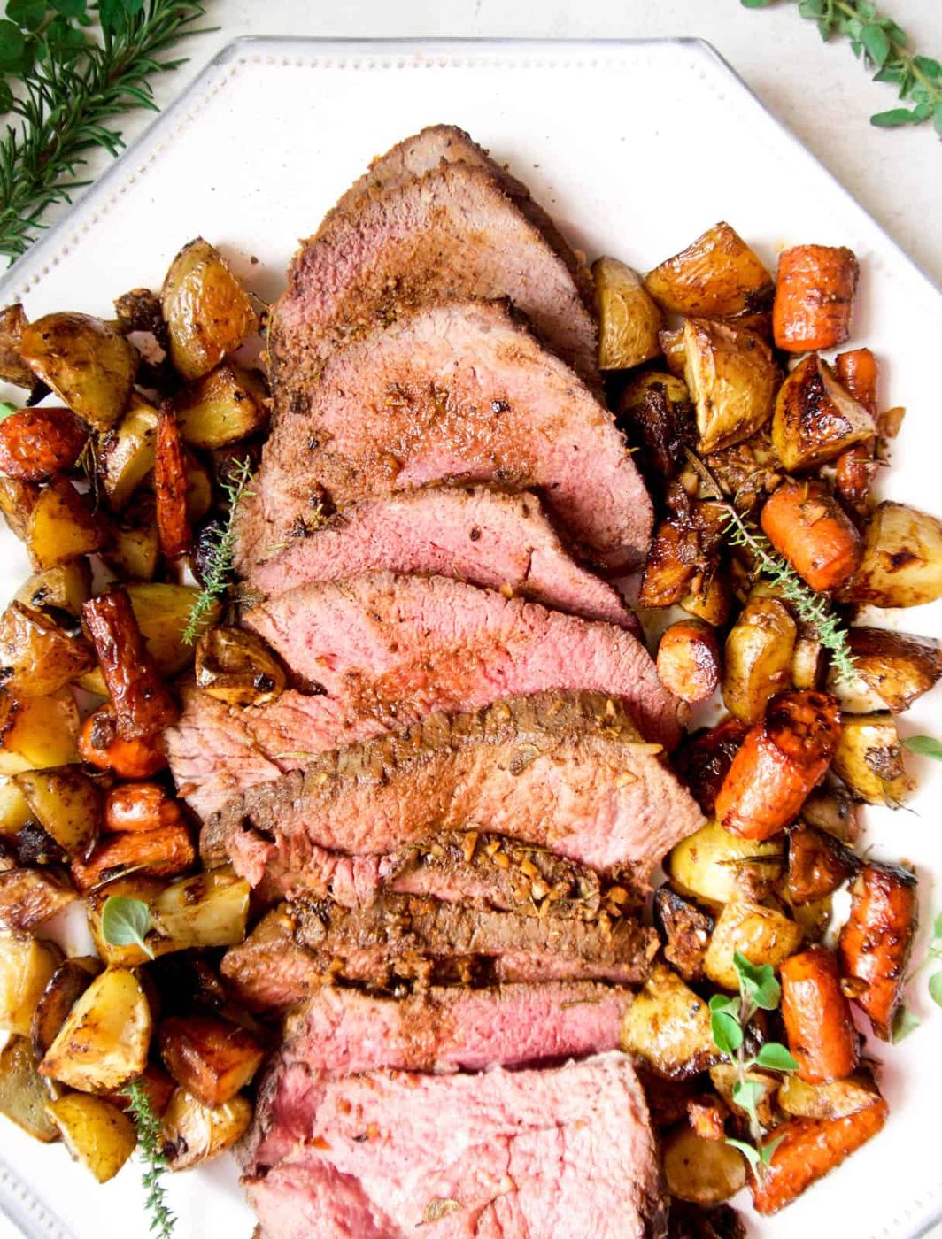 Slices of shoulder clod roast on a plate and surrounded by potatoes and carrots.