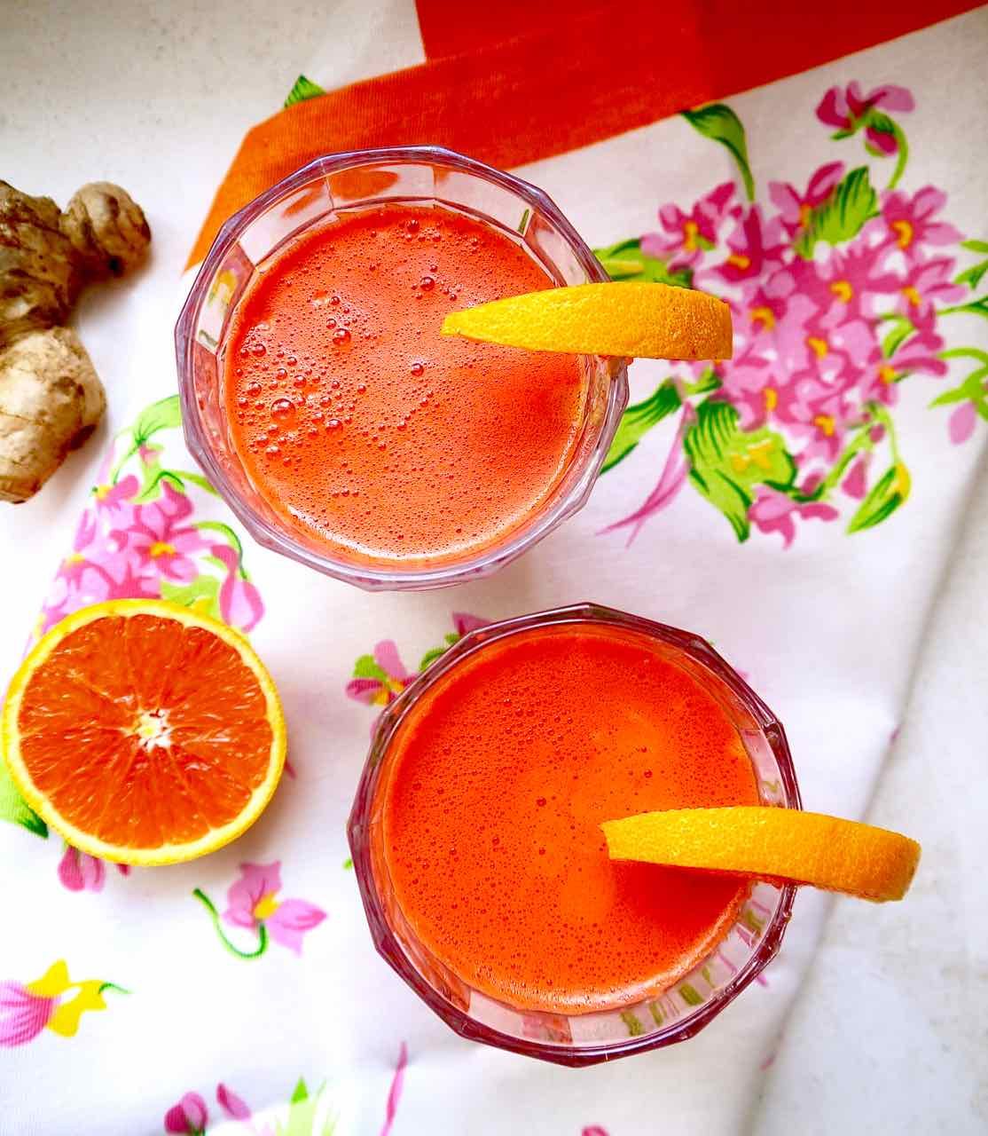 Apple Carrot Beet Ginger Juice in two cups with oranges on the rims.