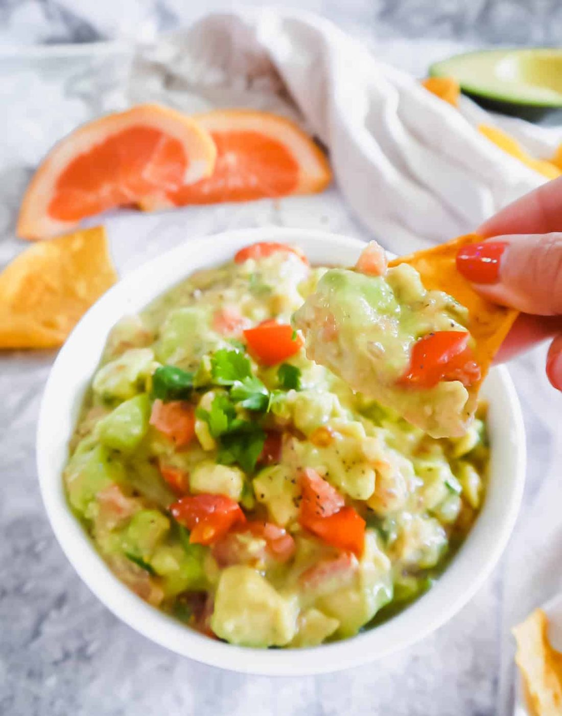 A chip being dunked into grapefruit guacamole.