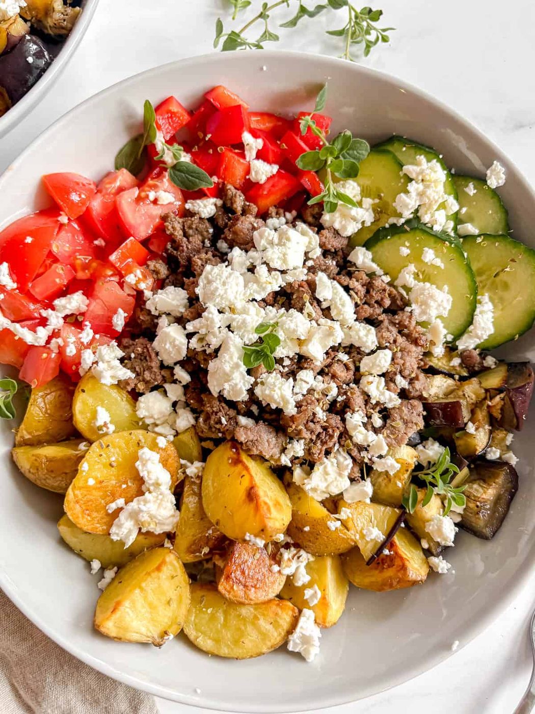 The greek bowls put together with potatoes, eggplant, cucumber, red pepper, tomato, ground beef, feta, oregano, and olive oil.