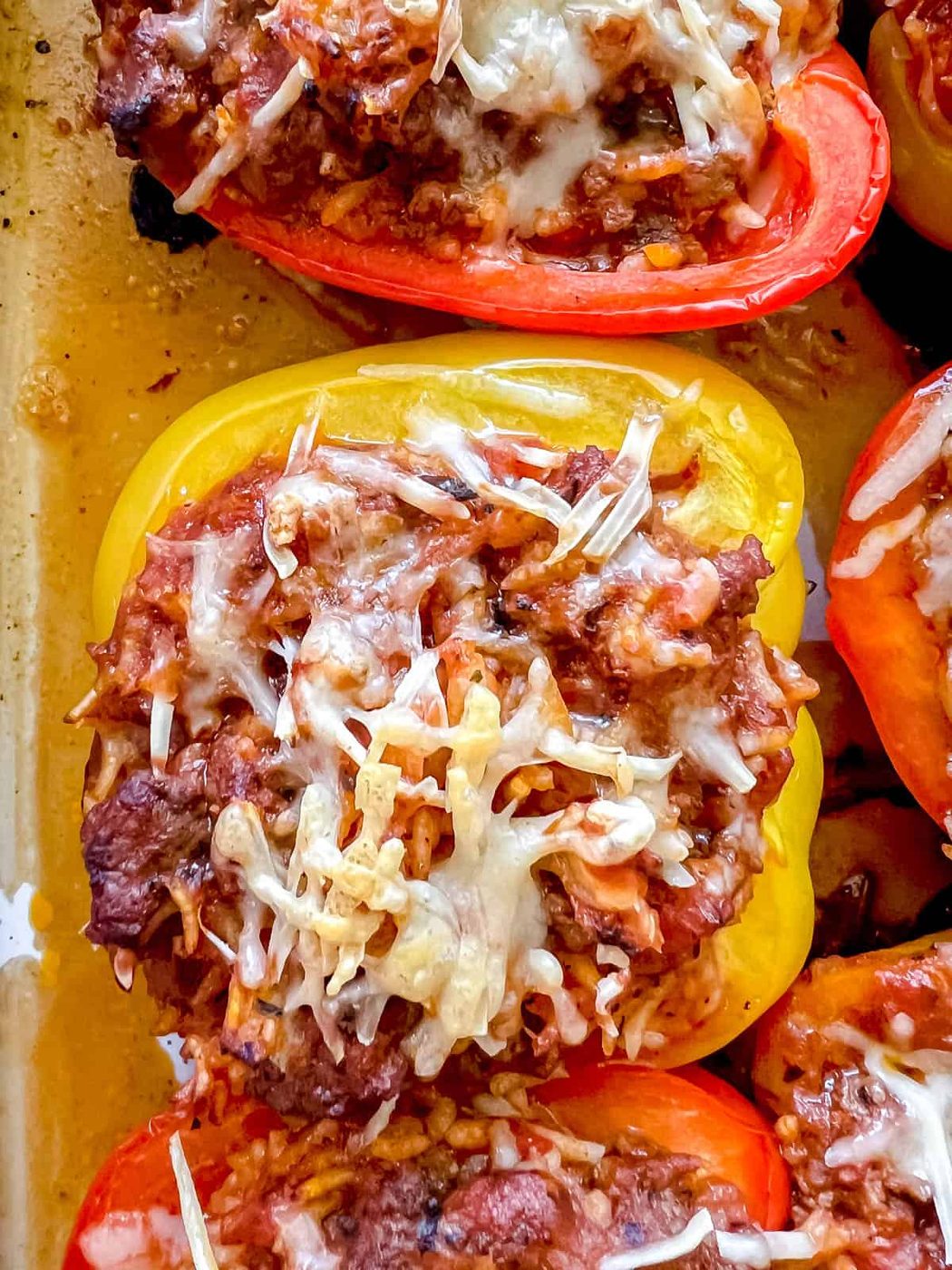 Up close photo of stuffed peppers with ground beef and rice with melted cheese on top.