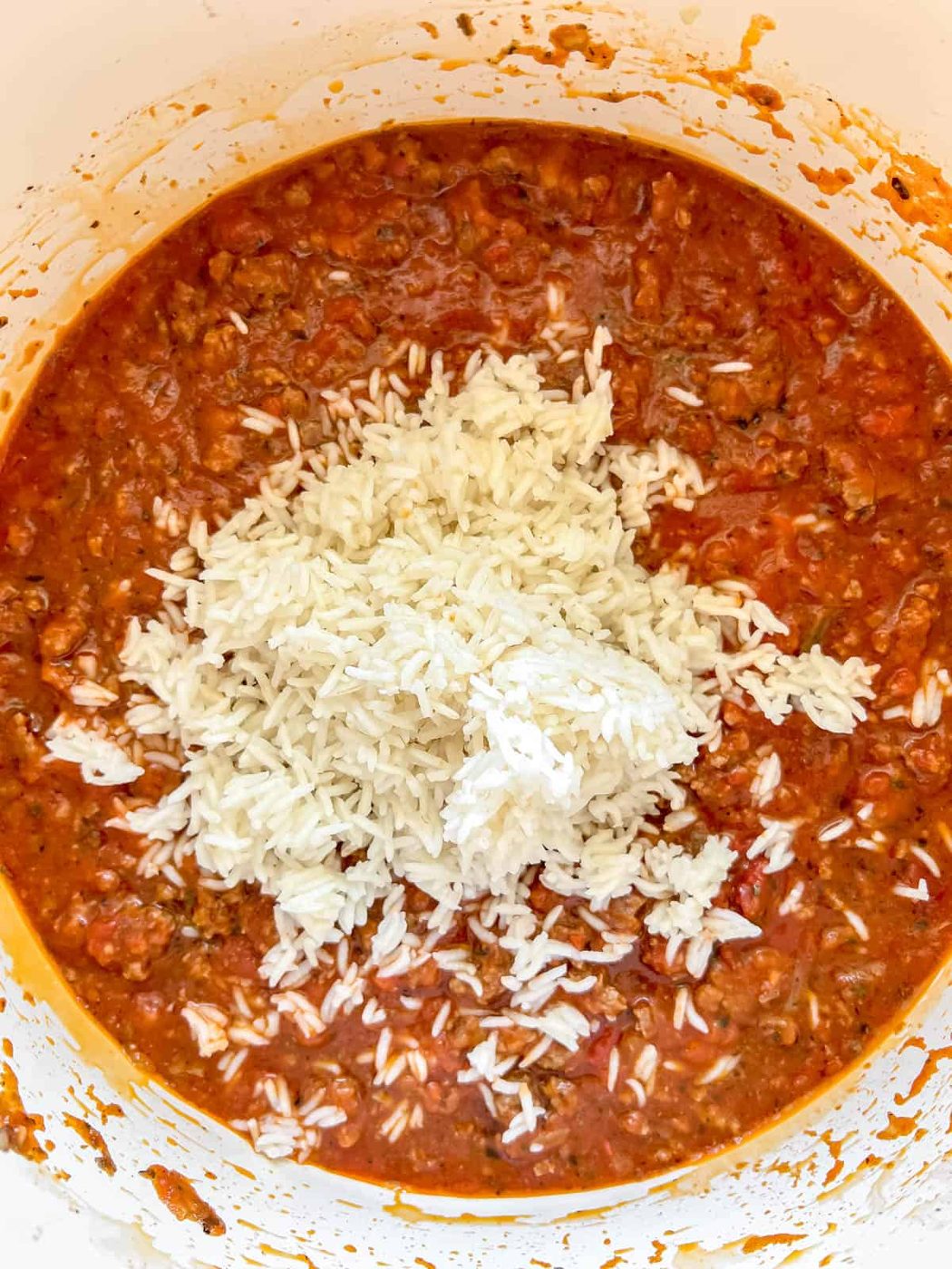 Cooked rice added to meat sauce in a pan.