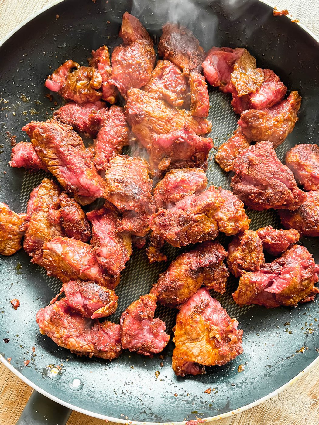 Seared stew meat in a frying pan.