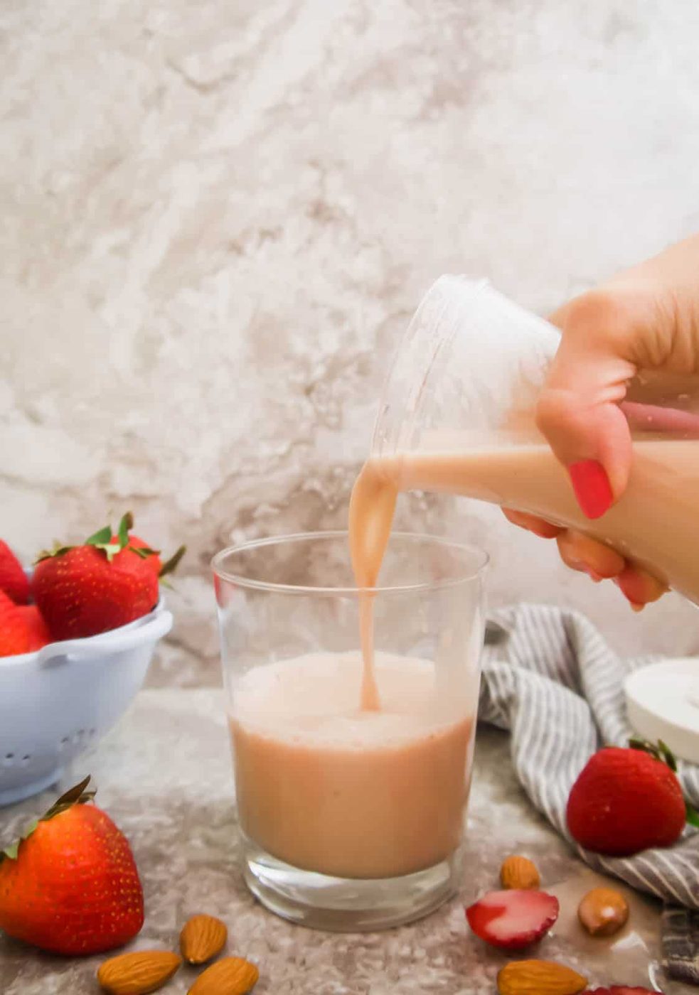 Pouring strawberry almond milk into a cup.