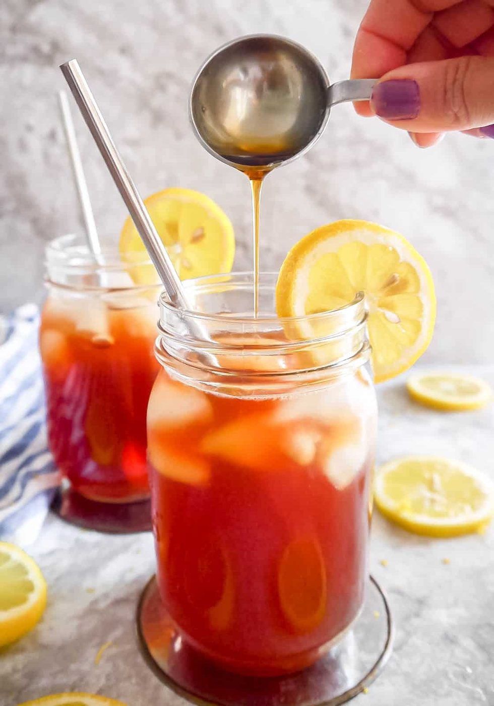 Lighter sweet tea in two cups with maple syrup being poured into a cup.