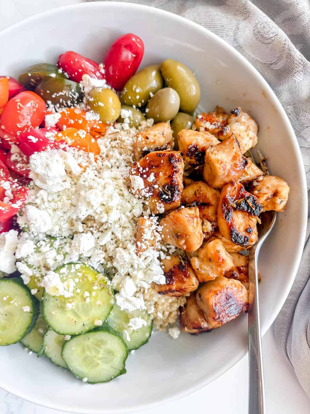 Maple lemon chicken in a bowl with feta, tomatoes, rice, and olives.