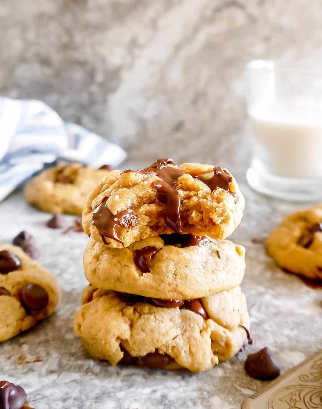 Three chocolate chip cookies stacked on each other with top cookie with bite taken out of it.