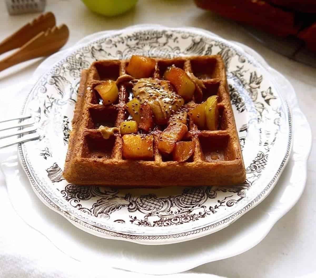 Paleo apple cinnamon waffles on a plate with apples on top.