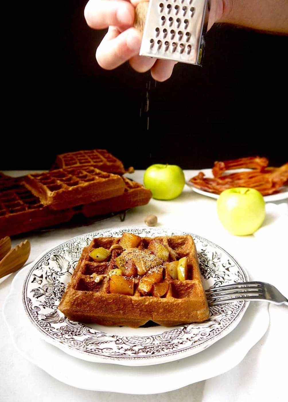 Lighter apple waffles with nutmeg being put on top.