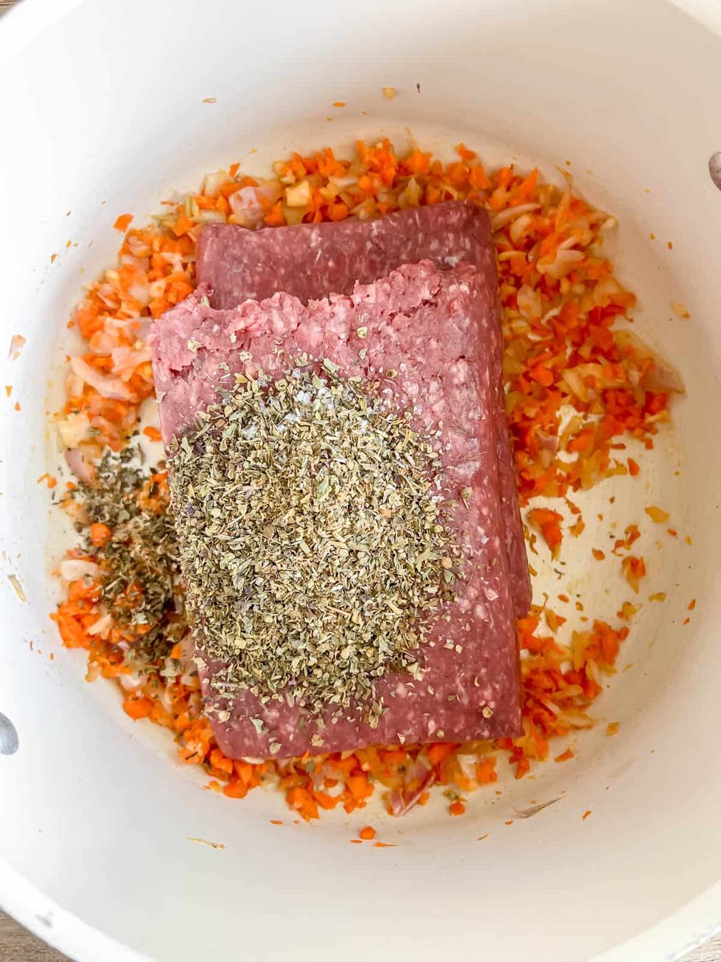 Bison and Italian seasoning on top of minced carrots, onions and garlic.