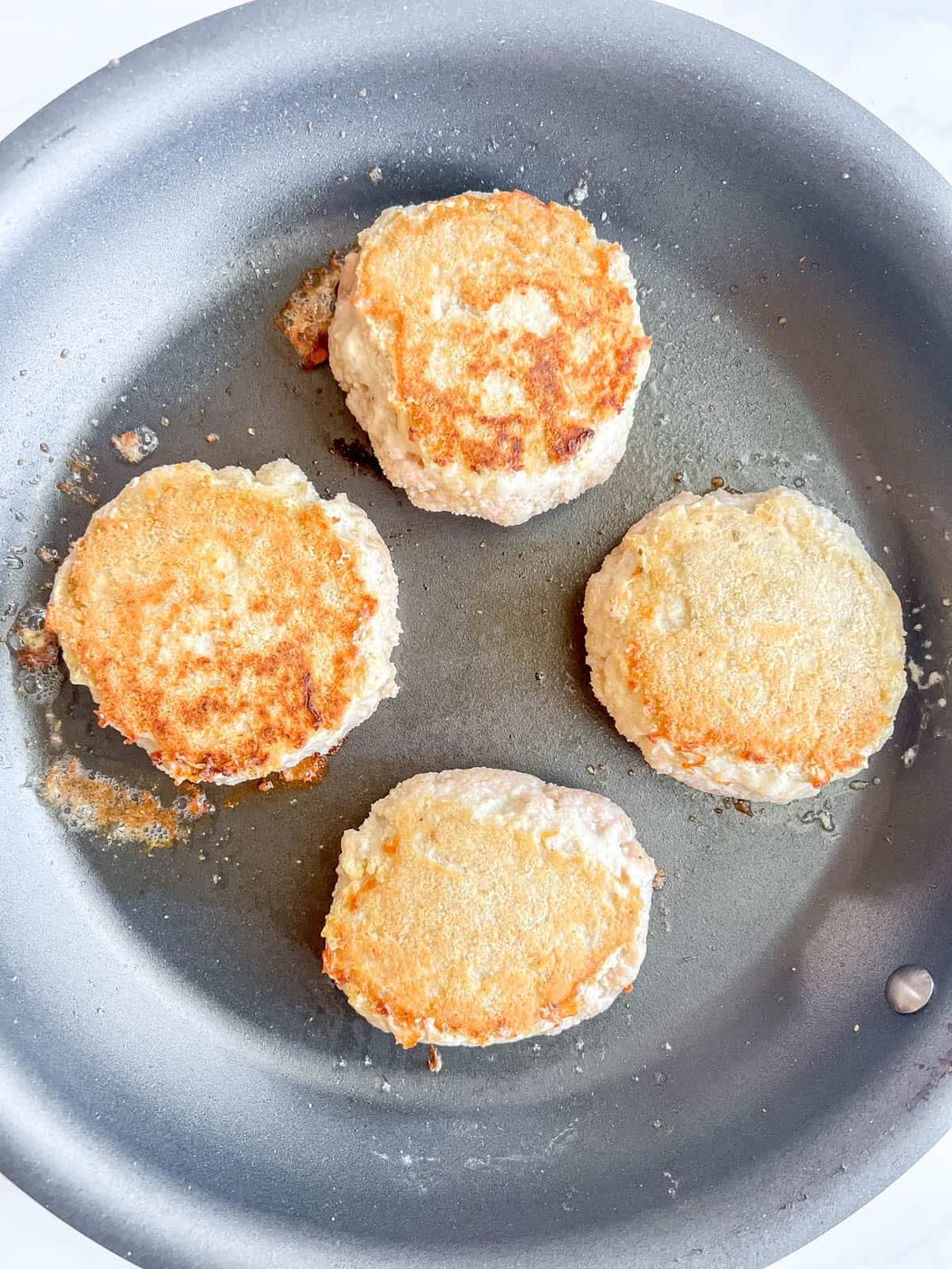 Chicken burgers flipped in a pan.