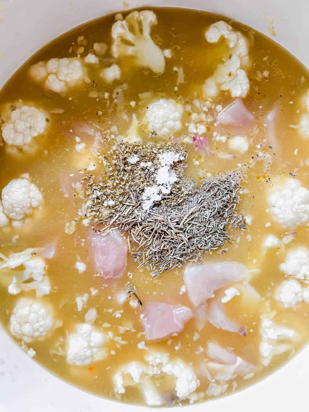 The broth, chicken and herbs and spices added to the pan.