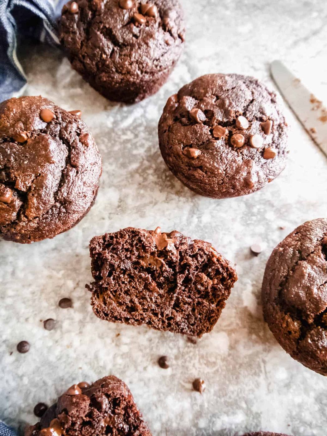 Banana chocolate gluten free muffins on a table. One is sliced in half.