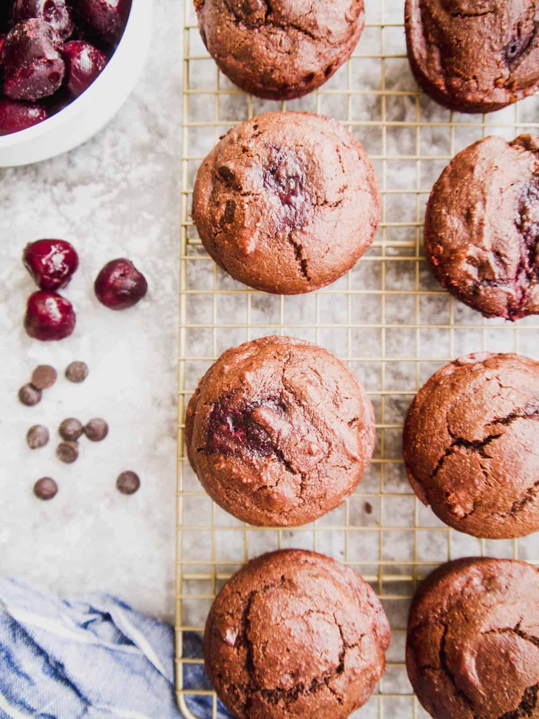 Lighter chocolate muffins with cherries cooling on drying rack.