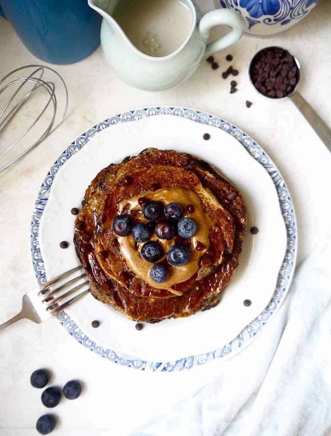 Lighter banana pancakes recipe on a plate with blueberries, and almond butter on top.