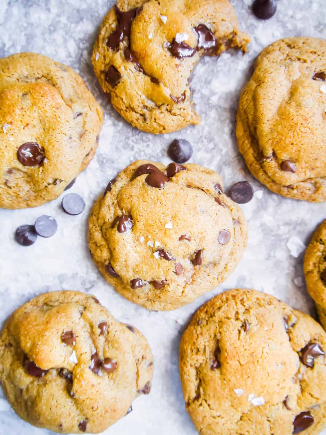 Several Chocolate Chip Cookies with Coconut Oil on a table with chocolate chips next to them.