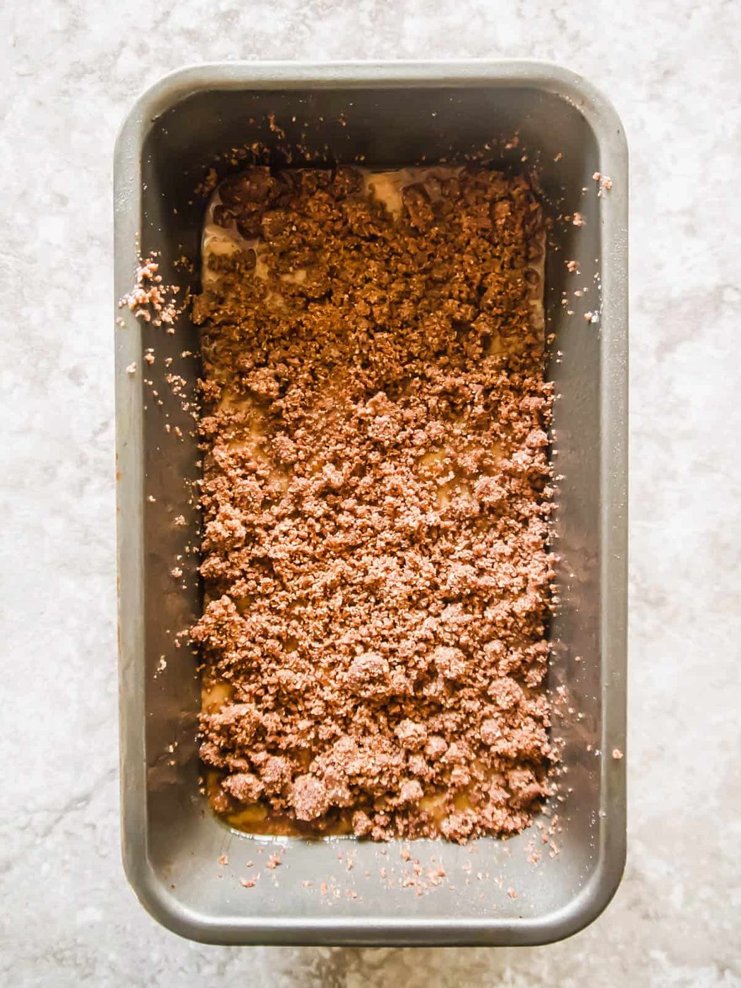 Banana bread coffee cake batter in a loaf tin with streusel on top.