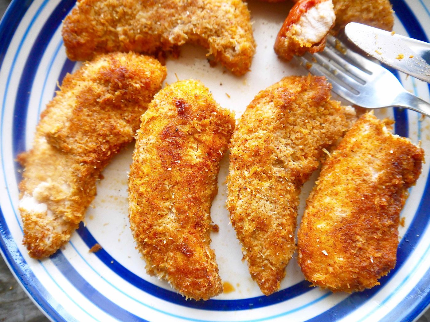 Chicken tenders with almond flour on a plate with a piece cut off.