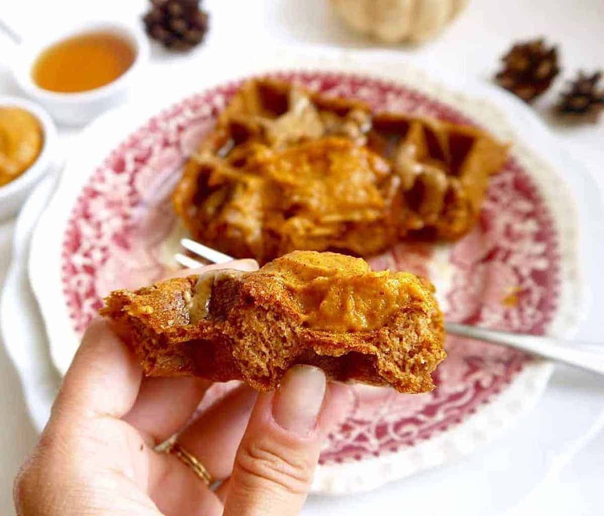 A bite of dairy-free pumpkin waffles in someone's hands.