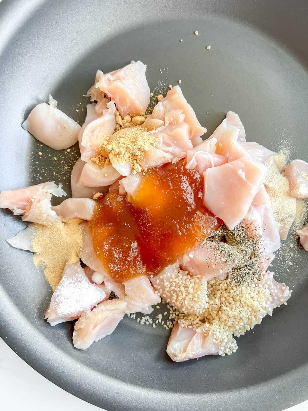 The raw chicken, honey, and sesame seeds in a pan.