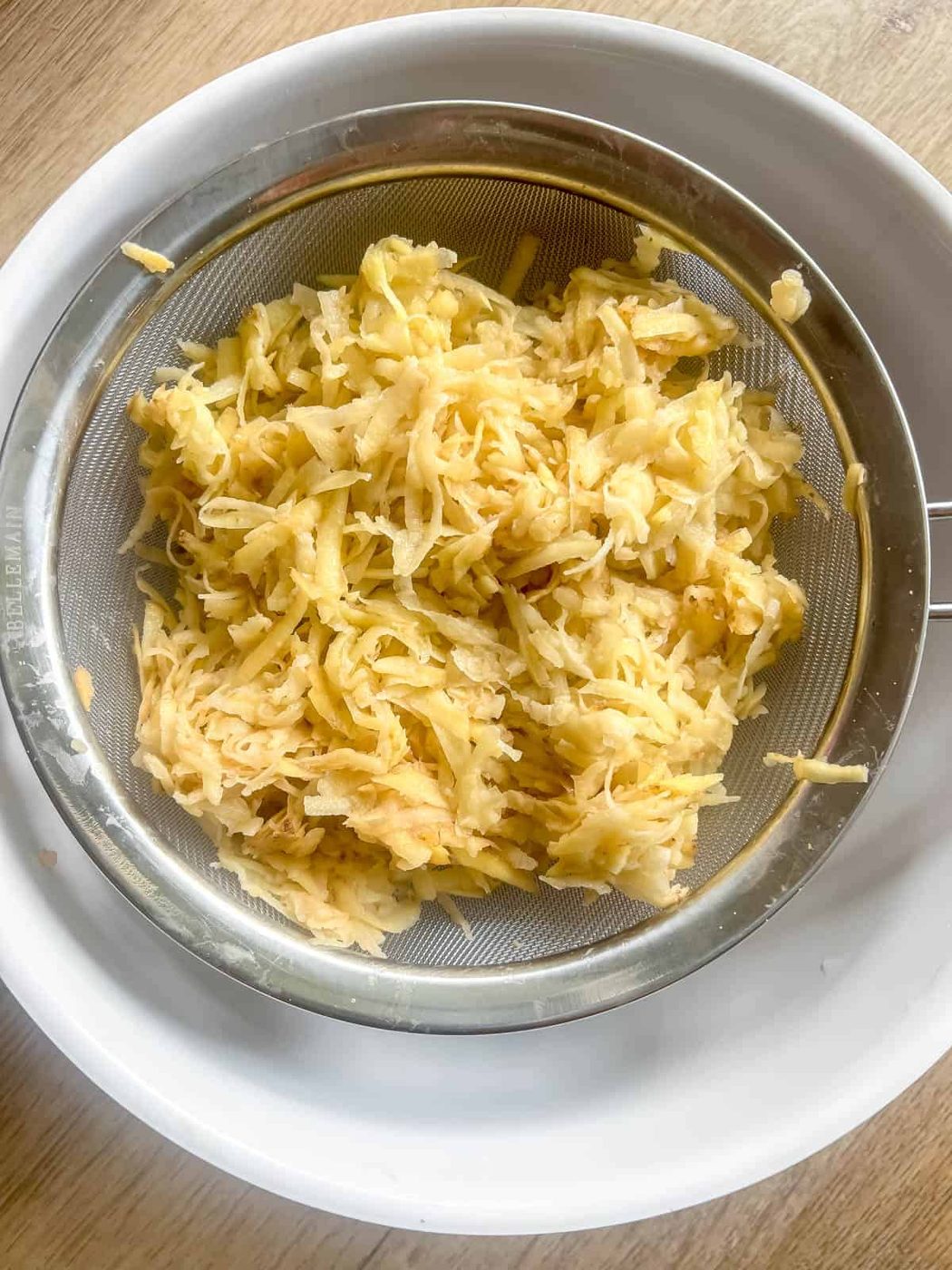 Straining shredded potatoes over a bowl.