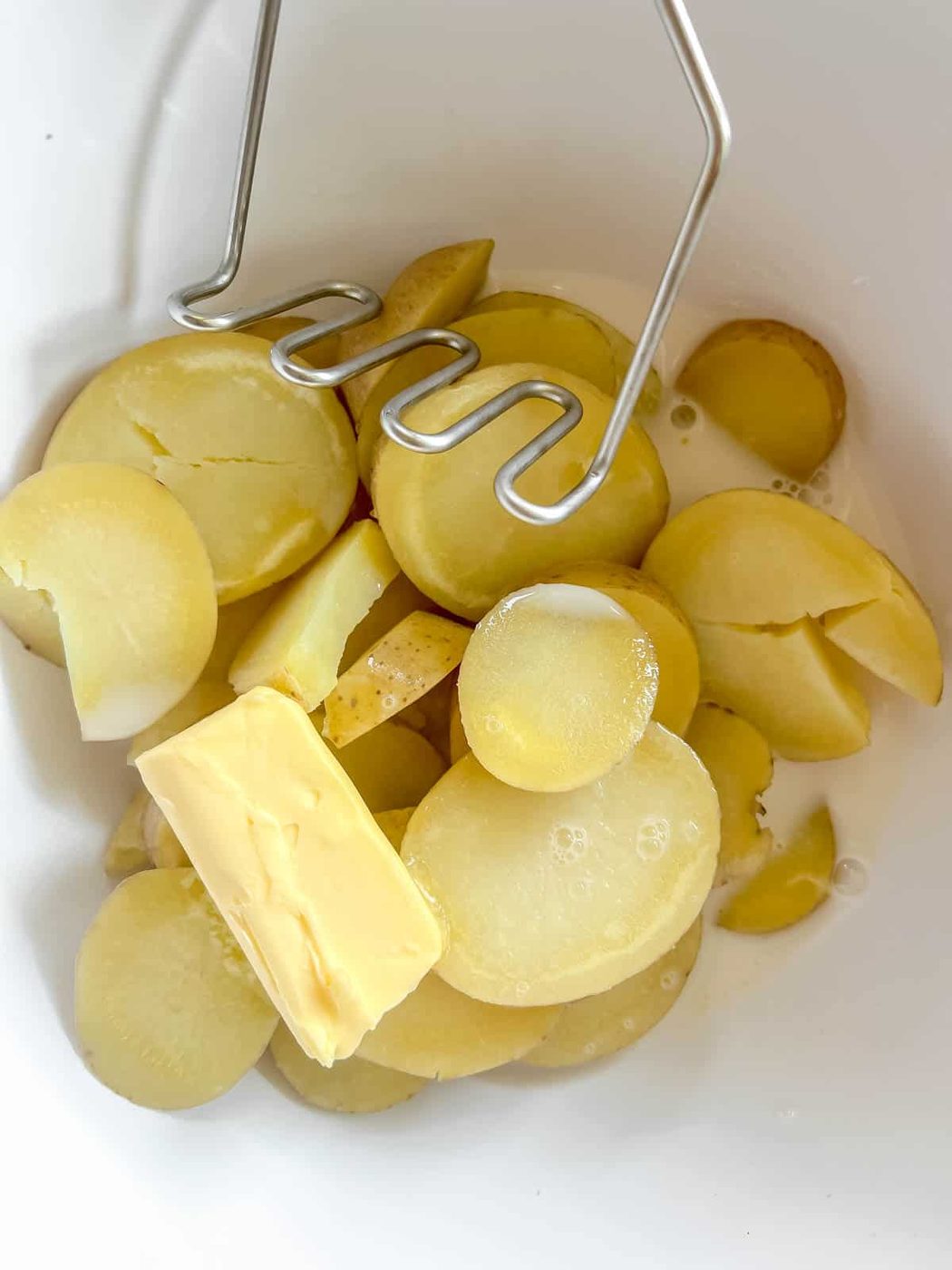 The boiled potatoes in a bowl with butter and almond milk ready to be mashed.