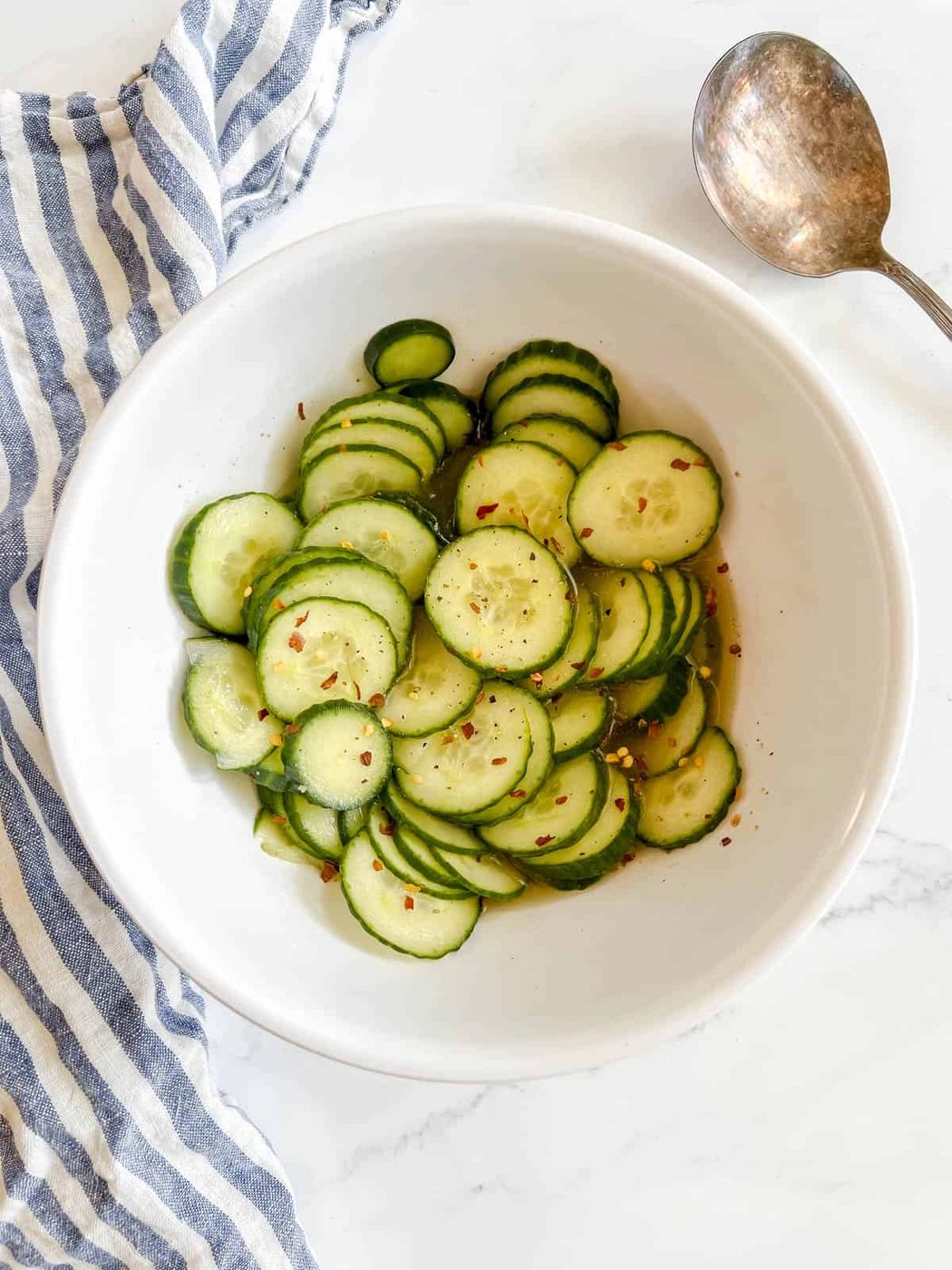 Fast asian pickled cucumbers in a bowl with crushed red pepper on top.