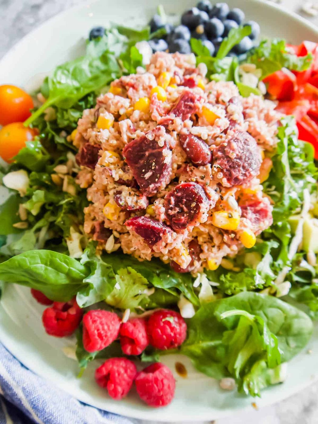Tuna quinoa salad on a plate with veggies and fruit.