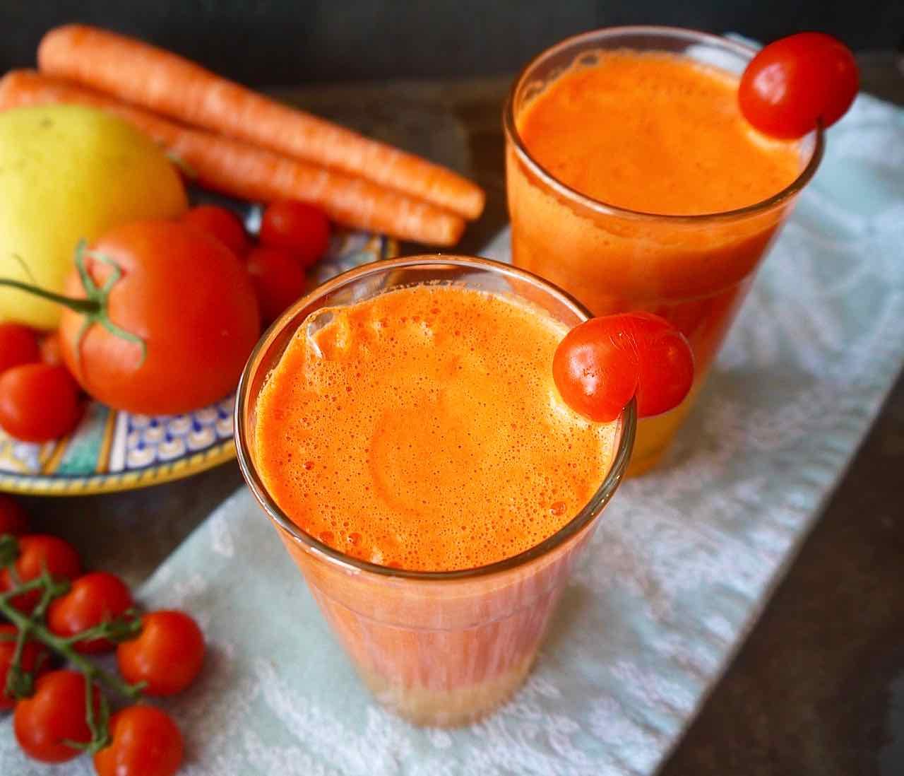 Side angle of orange carrot tomato juice in two glasses.