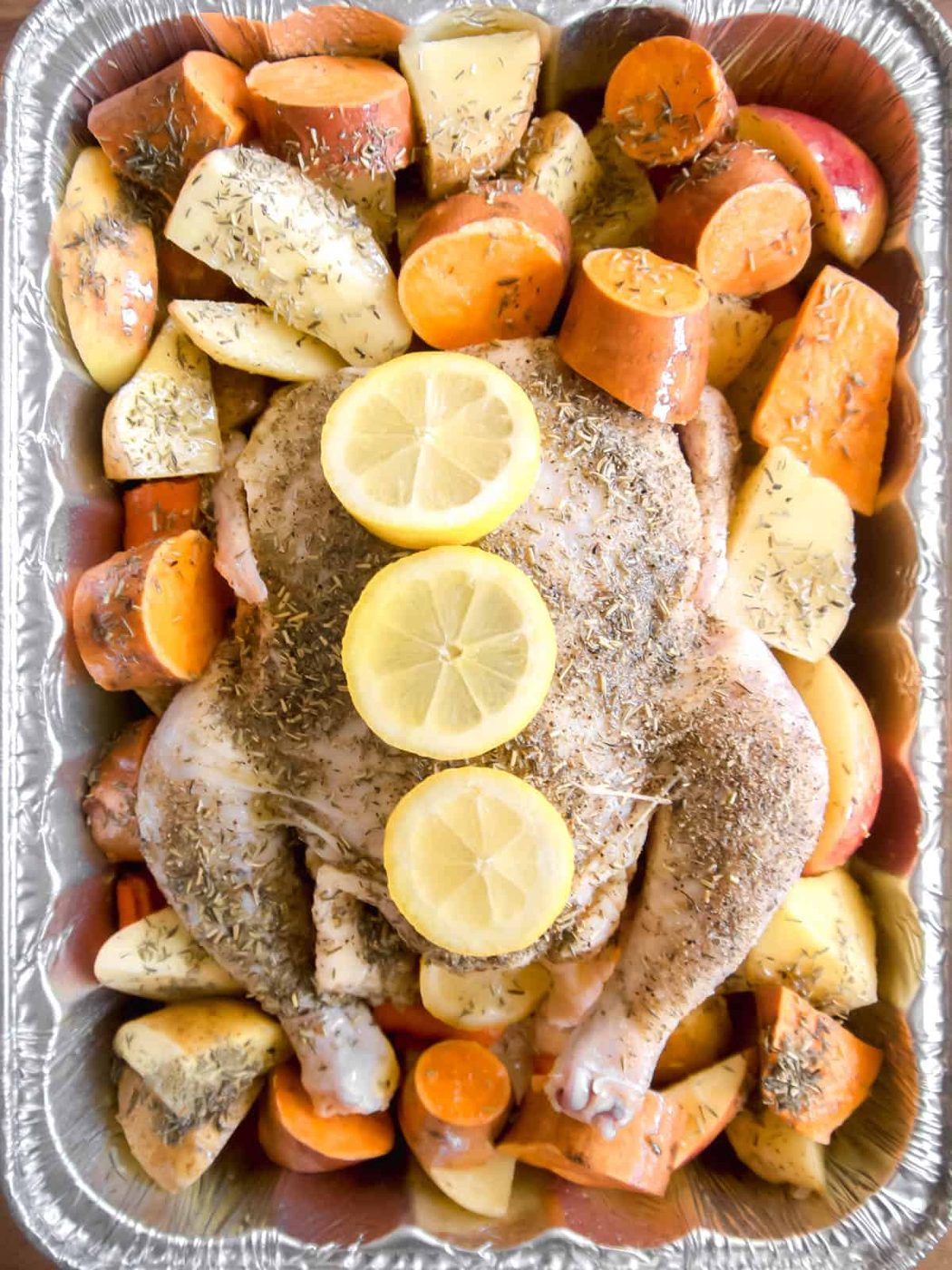 Potatoes and apples surrounding the raw chicken.