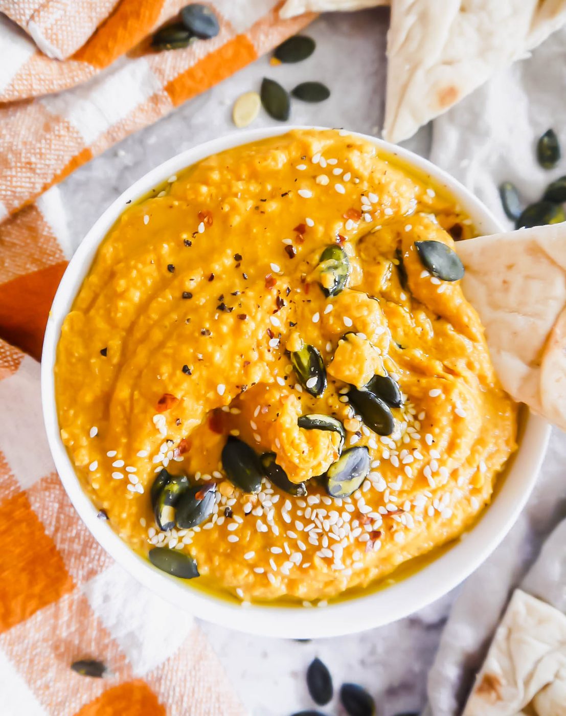 Pita dunked into pumpkin hummus in a bowl.
