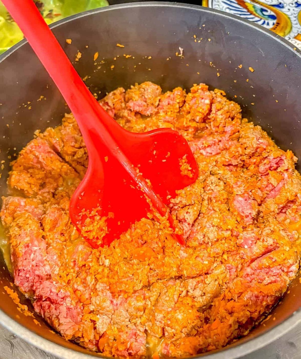 Using a meat masher to break up the beef.