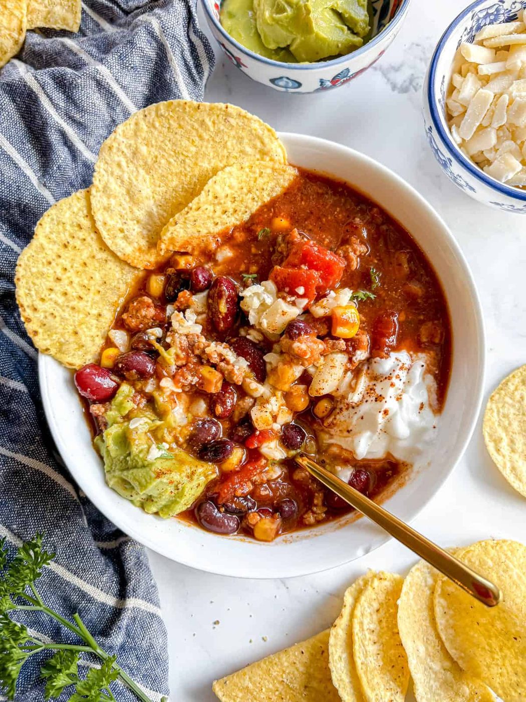 Lighter turkey chili in a bowl with a spoon mixing all the toppings in it.