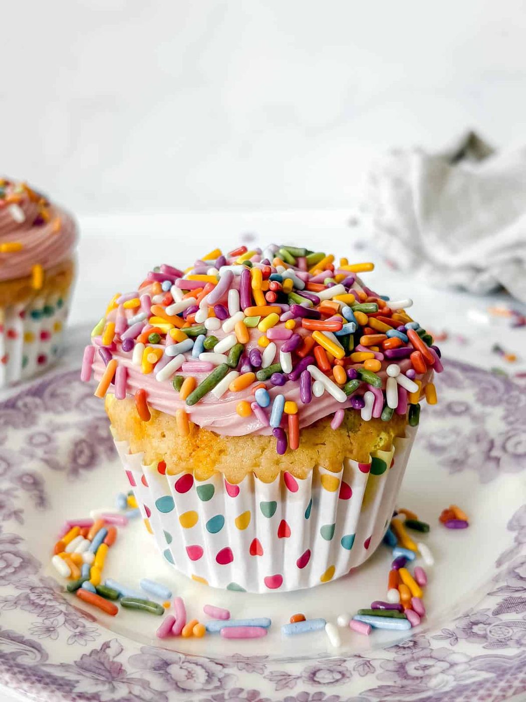 A funfetti cupcake with pink frosting and lots of sprinkles on top.