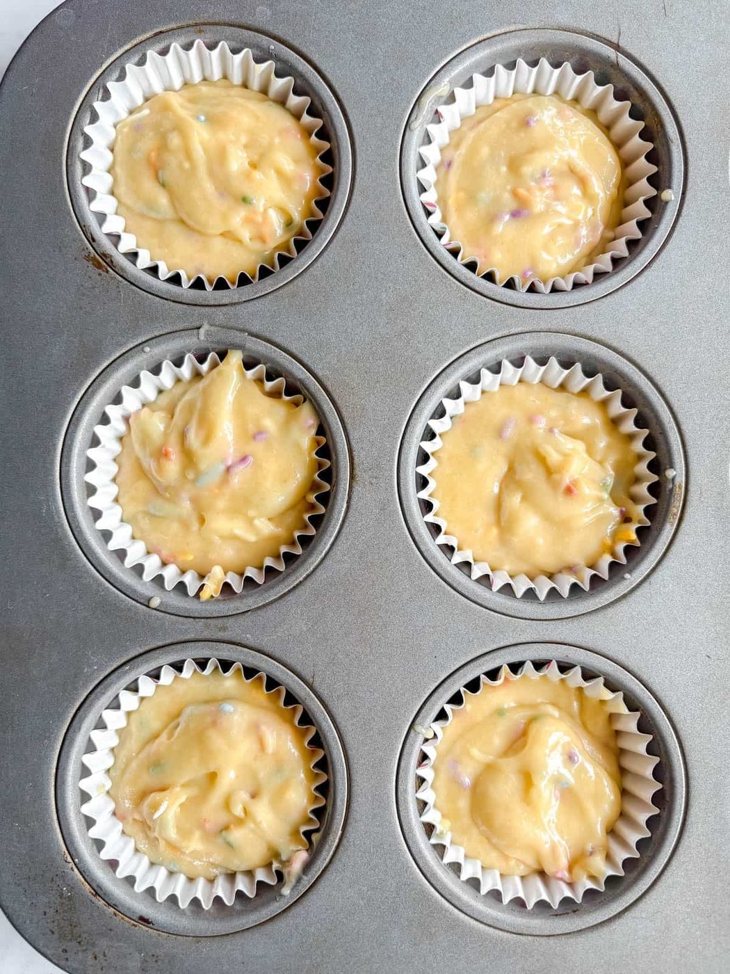 6 cupcakes filled with funfetti batter before baking.